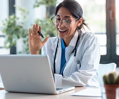 Physician smiling and waving while looking at the laptop