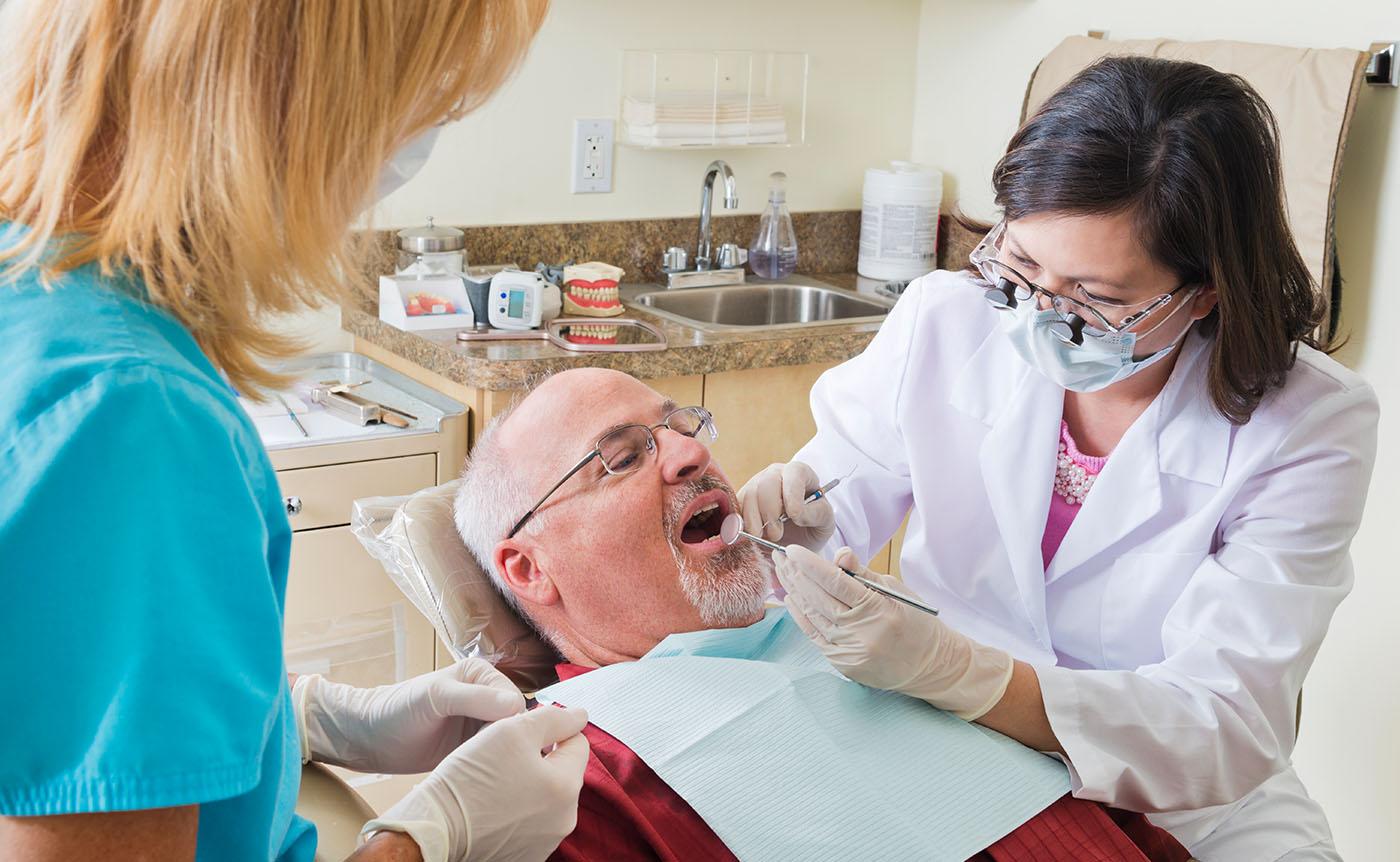 Older man in dental chair, female dentist and female assistant